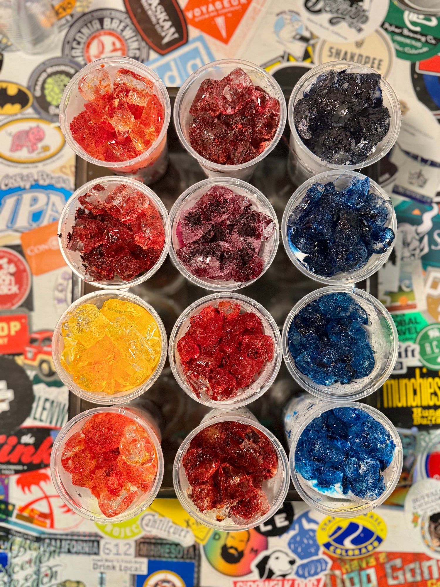 Assorted ice dye swatch samples in small containers on a colorful background with stickers.