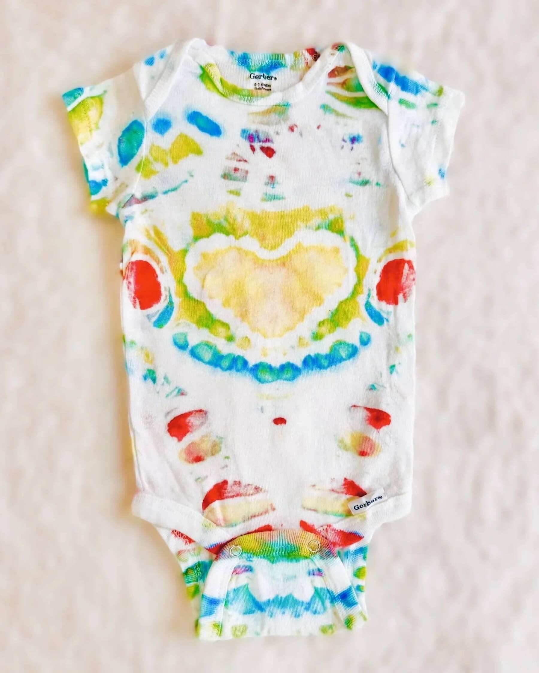 Multicolor heart ice-dyed baby onesie in daylight on white background