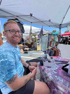 Man sitting at an outdoor market stall wearing a hand ice dyed blue tee