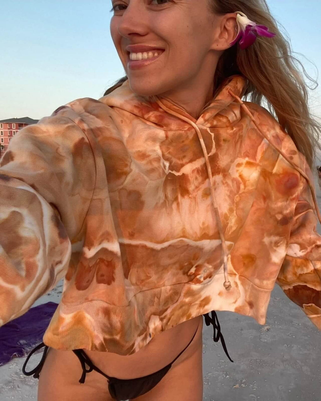 Woman wearing a hand ice dyed orange and brown cropped hoodie on a beach.