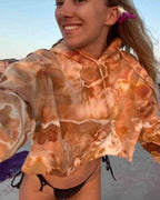 Woman wearing a hand ice dyed orange and brown cropped hoodie on a beach.