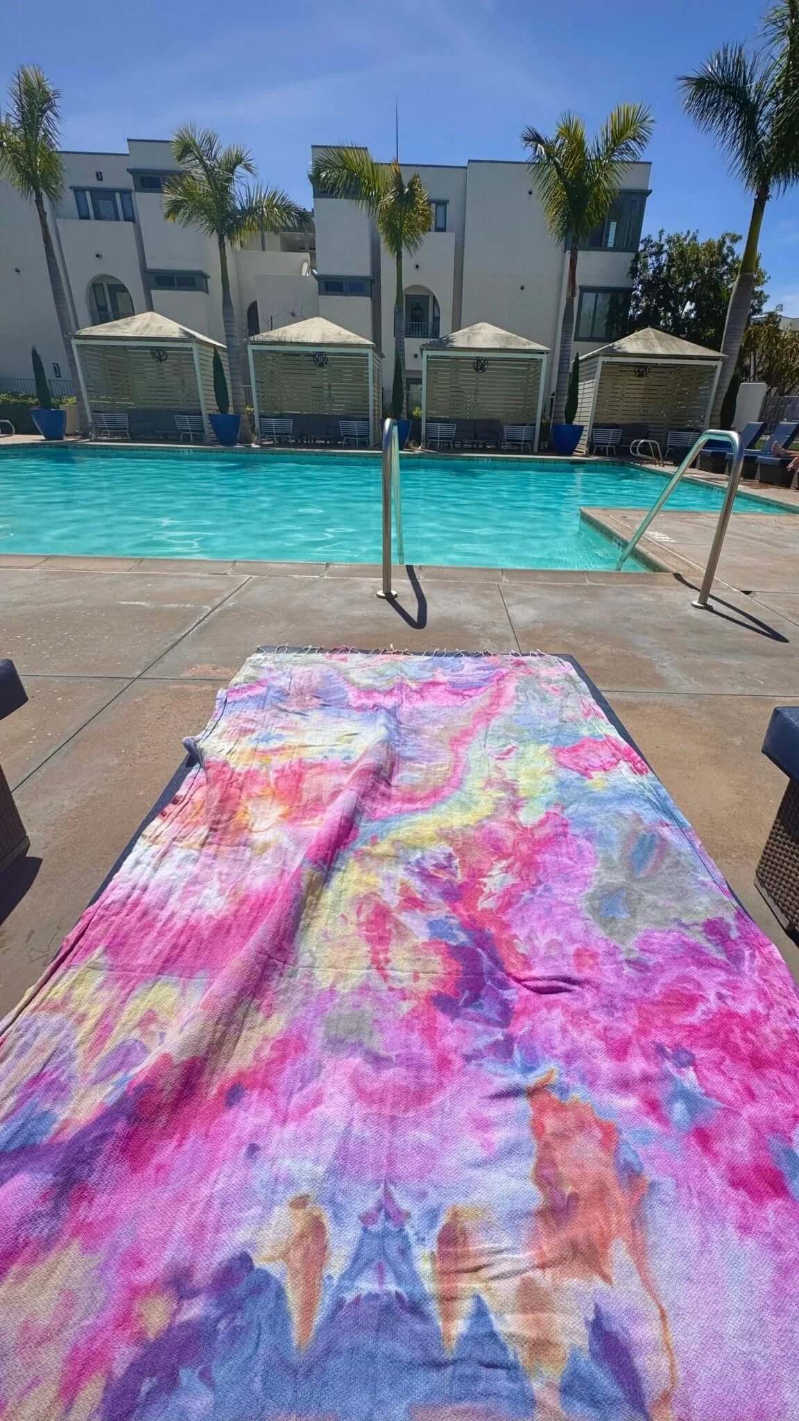 Colorful ice-dye towel on a poolside with a pool and building in the background
