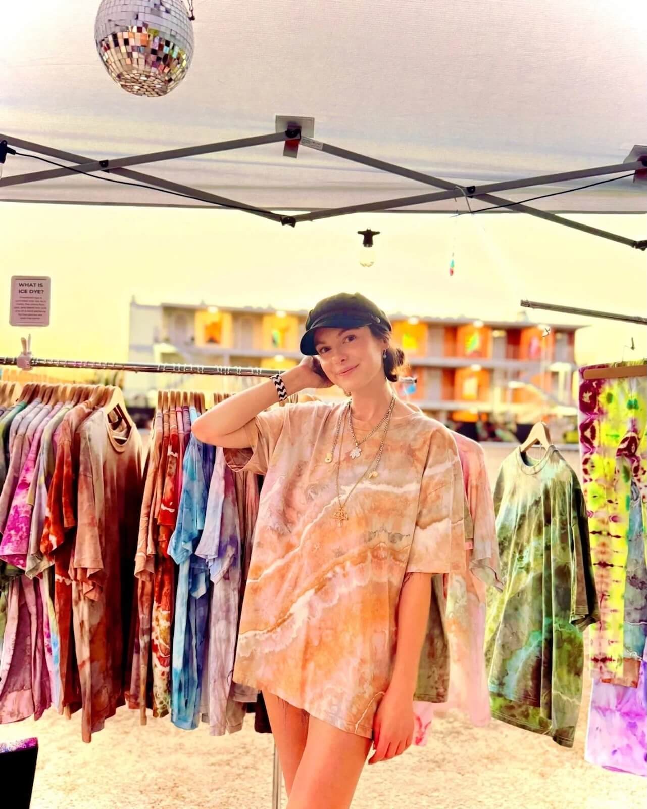 Woman wearing a tie-dye oversized shirt at the OB Tie Dye booth with colorful garments on racks.