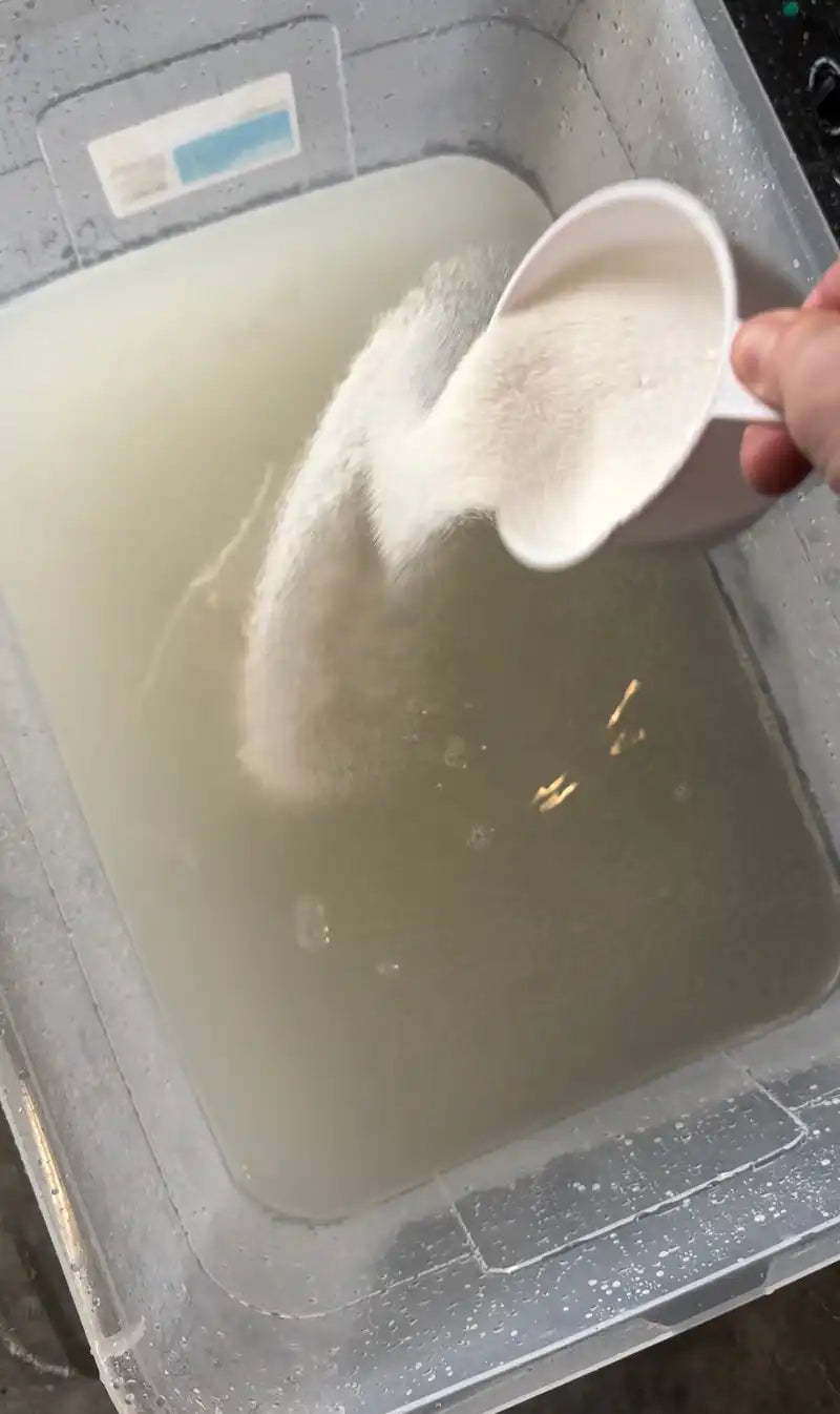 Soda ash being poured into a water tub to prep fabric for the ice-dye process.