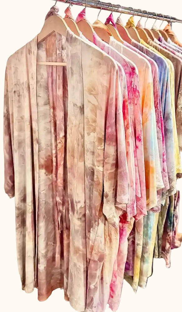 Rack of assorted OB Tie Dye kimonos in soft pastel and earth-tone ice-dye palettes hanging on wooden hangers.