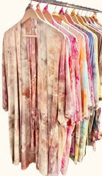 Rack of assorted OB Tie Dye kimonos in soft pastel and earth-tone ice-dye palettes hanging on wooden hangers.