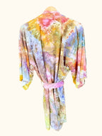 Back view of hand ice dyed colorful kimono robe hanging against a green leafy background