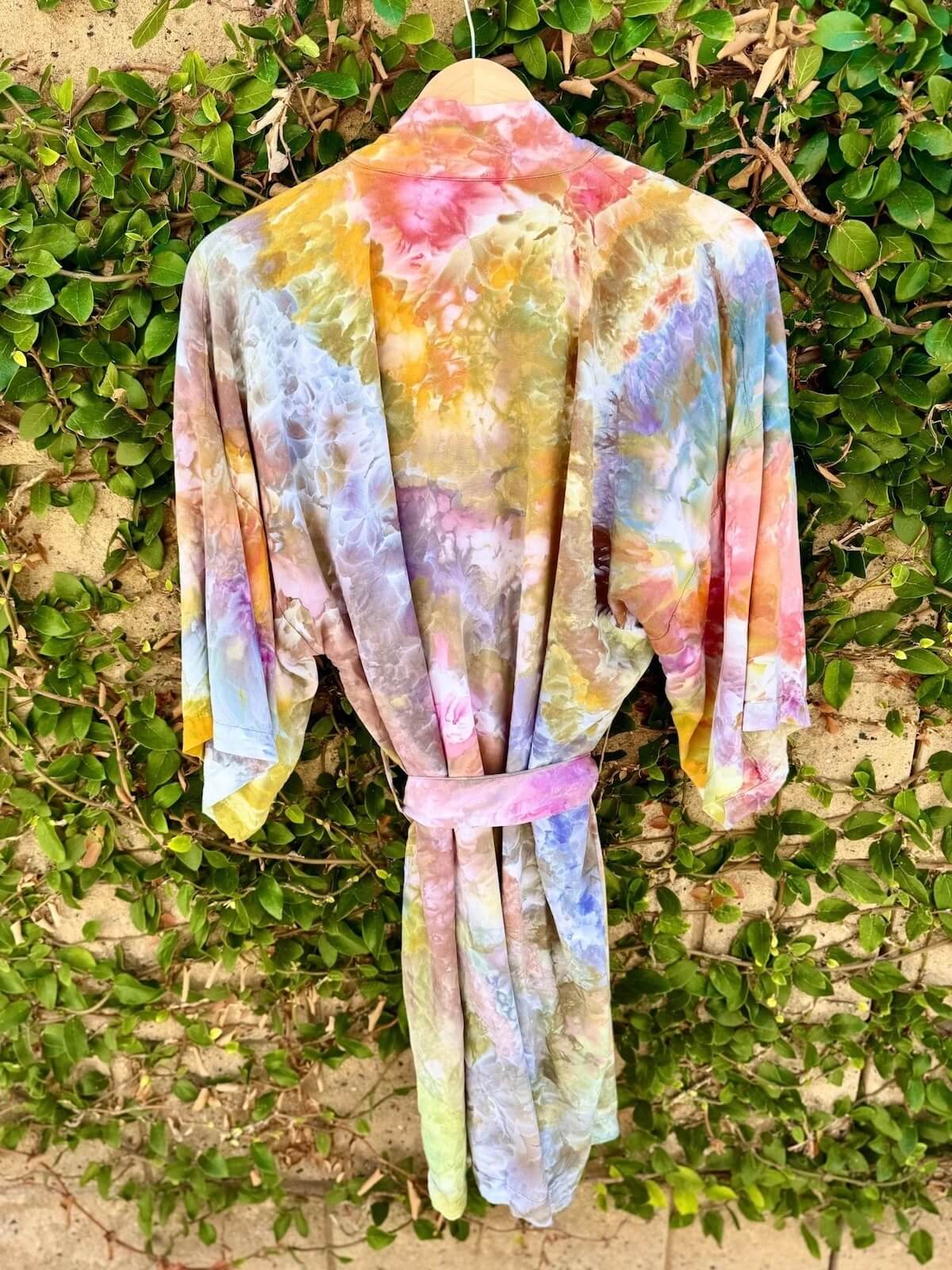 Back view of hand ice dyed colorful kimono robe hanging against a green leafy background