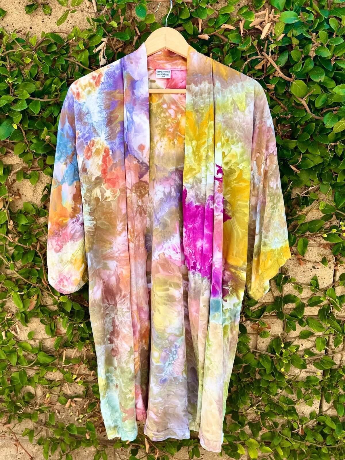 Open front view of hand ice dyed colorful kimono robe hanging against a green leafy background