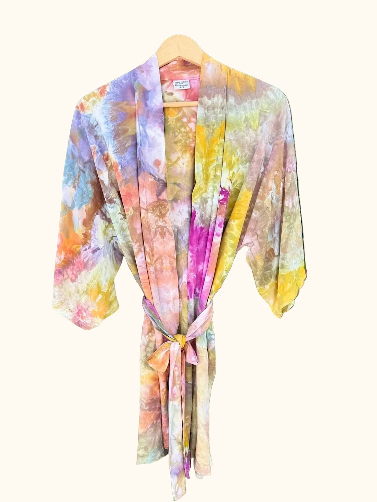 Front view of hand ice dyed colorful kimono robe hanging against a green leafy background