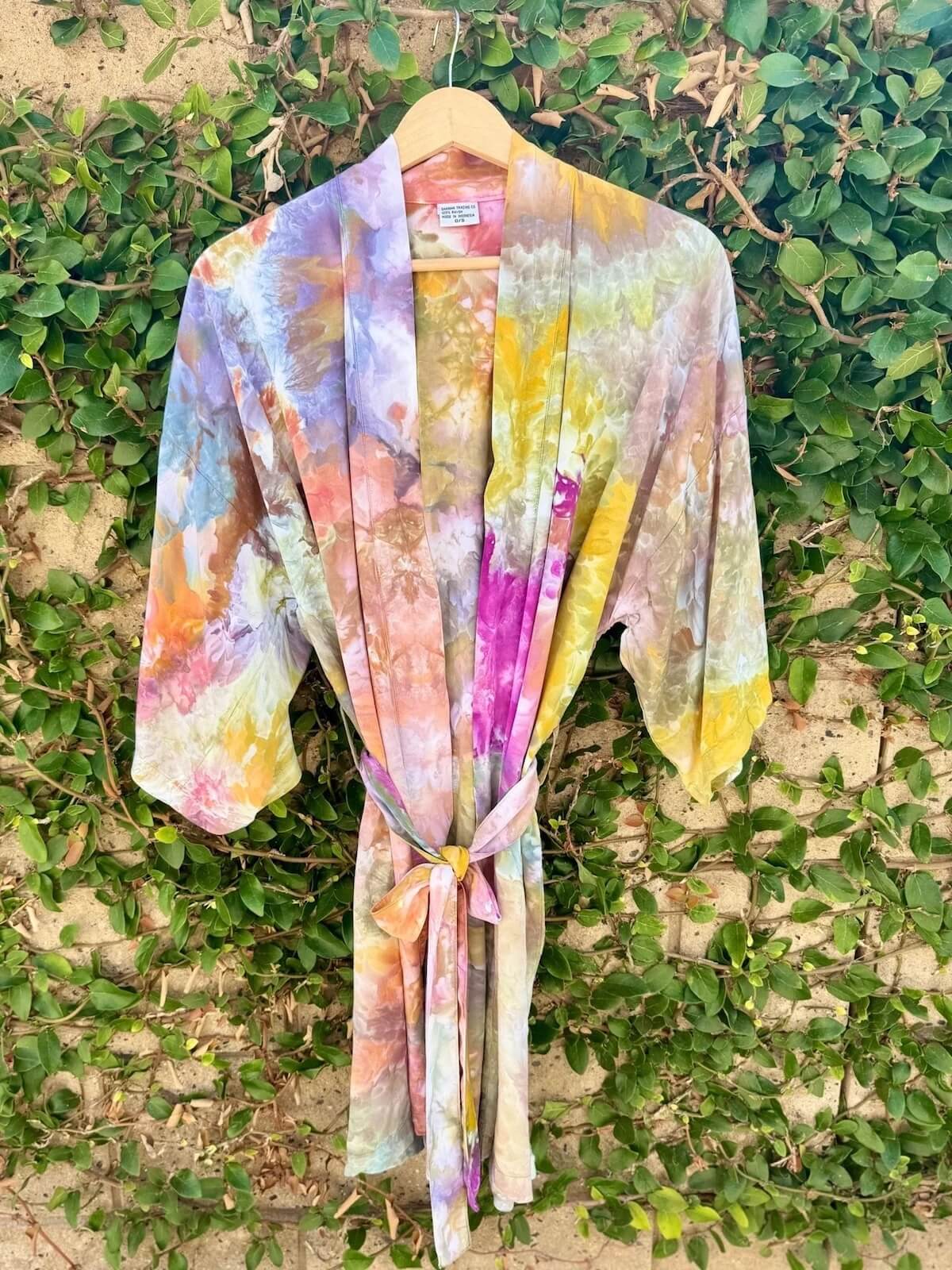 Front view of hand ice dyed colorful kimono robe hanging against a green leafy background