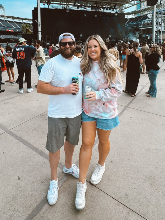 Two people standing together at a music festival with a stage in the background. The woman is wearing an OB Tie Dye Unisex Hand Dyed Hoodie.